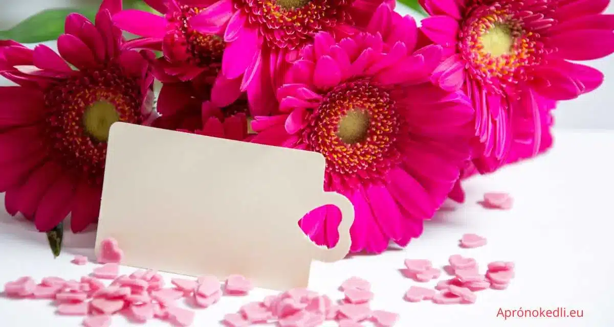 Baba születése gratuláció képeslap. Tárgyak: A képen szintén rózsaszín virágok (valószínűleg gerberák) láthatók, amelyek mellett egy üres kártya található, amelynek egyik sarkában egy szív kivágás van. Háttér: A virágok és a kártya előtt apró rózsaszín szívek vannak szétszórva, amelyek további díszítést adnak a képhez. Színek: A kép fő színei az élénk rózsaszín (virágok és szórt szívek) és a fehér (kártya).