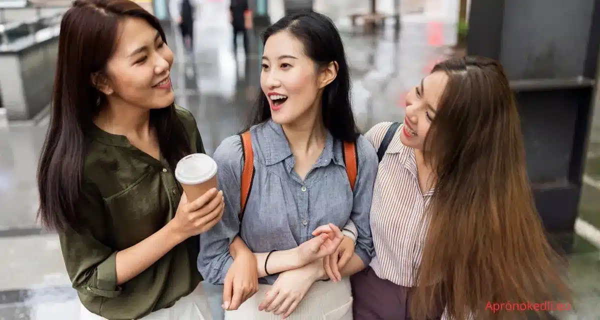 Barát idézet. Három fiatal nő sétál az utcán és beszélget. Az egyikük (bal oldalon) egy zöld felsőt és fehér nadrágot visel, és egy kávét tart a kezében. A középső nő egy világoskék inget és hátizsákot visel, mosolyogva néz a bal oldali nőre. A jobb oldali nő hosszú hajjal és csíkos inggel, szintén mosolyogva néz a középső nőre. Mindhárman barátságosan átkarolják egymást, és úgy tűnik, hogy jól érzik magukat együtt. Az utca, ahol sétálnak, nedvesnek tűnik, talán eső után, és városi háttér látható homályosan.