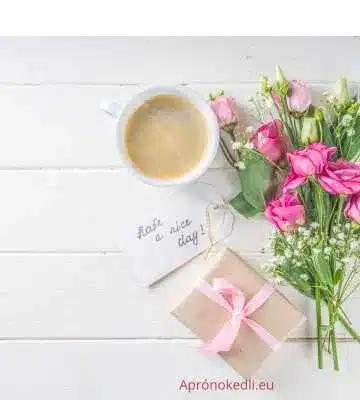 Reggeli köszöntések. A képen egy csésze kávé látható egy fehér fából készült asztalon. A kávé mellett egy kis csokor rózsaszín és fehér virág található. A kávé és a virágok mellett egy barna papírba csomagolt ajándék, rózsaszín szalaggal átkötve. Egy kis kártya van elhelyezve a kávé mellett, amelyen az áll: "Have a nice day!" (Legyen szép napod!)