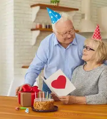 Szerelmes szülinapi köszöntő. Ez a kép egy idősebb párt ábrázol, akik egy születésnapi ünnepségen vesznek részt. Mindketten ünnepi sapkát viselnek. A férfi egy ajándékot és egy szívvel díszített kártyát ad át a nőnek, míg a nő mosolyogva nézi a kártyát. Az asztalon egy torta látható gyertyákkal, ami szintén az ünneplés részét képezi.