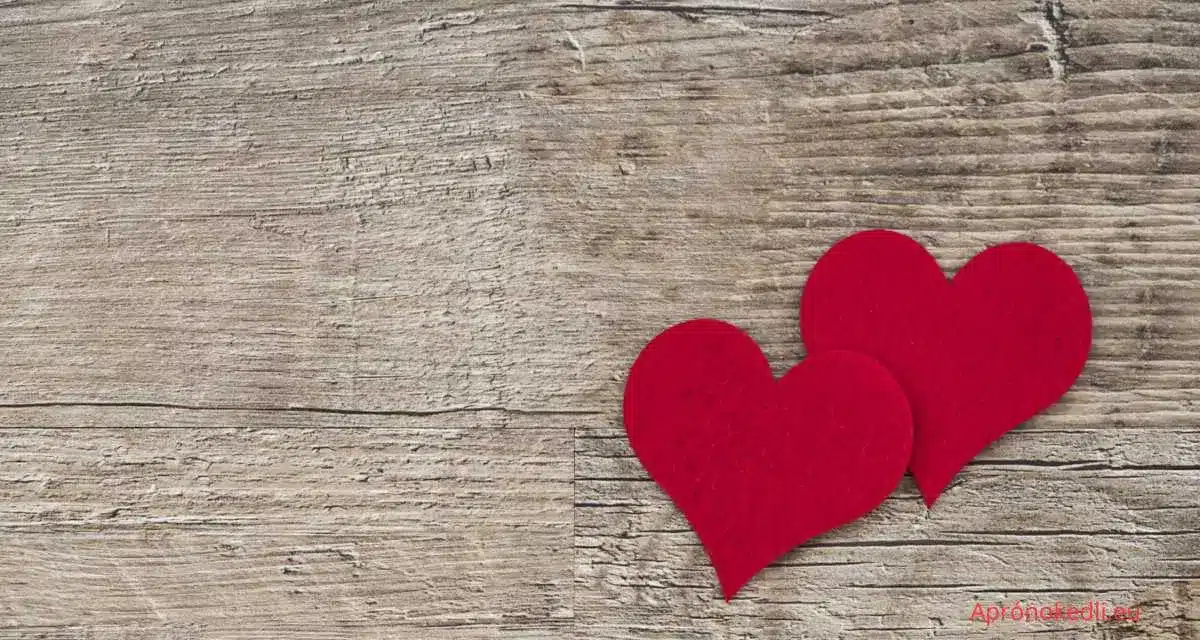 Szerelmes szülinapi köszöntő. A képen egy fa háttér előtt öt piros szív látható. A szívek szépen elrendezve helyezkednek el, és romantikus hangulatot árasztanak. A fa háttér természetes hatást kölcsönöz a képnek, és kontrasztot alkot a piros szívek élénk színével.