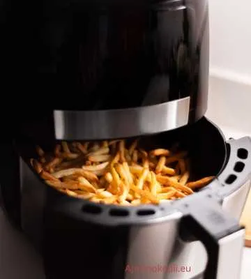 Ezen a képen egy légsütő (air fryer) látható, amelyből éppen készülnek a hasábburgonyák. A légsütő tálcája ki van húzva, és a tálcában aranybarnára sült hasábburgonyák vannak. A légsütő fekete színű, modern dizájnú.